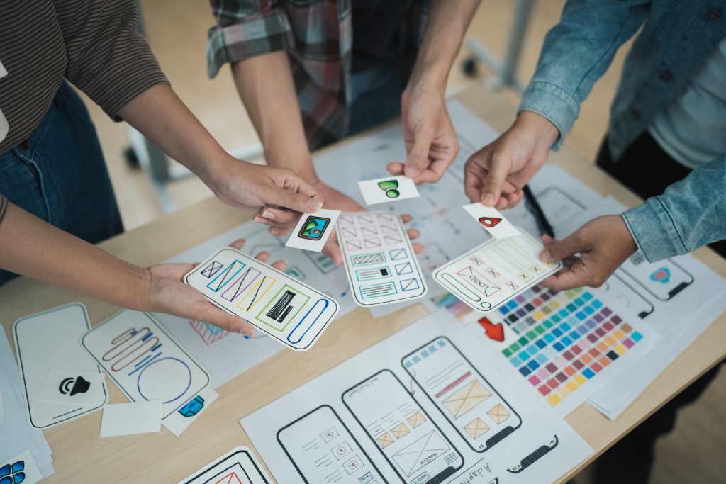 asian team ux developer ui designer brainstorming about mobile app interface wireframe design table with customer brief color code modern office
