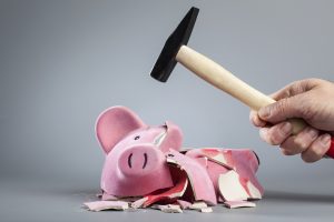 cropped image hand breaking piggy bank using hammer against gray background