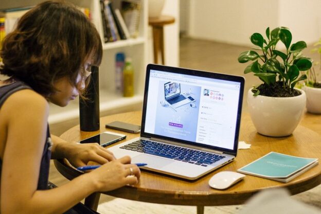Person reviewing a web page on a laptop and taking notes